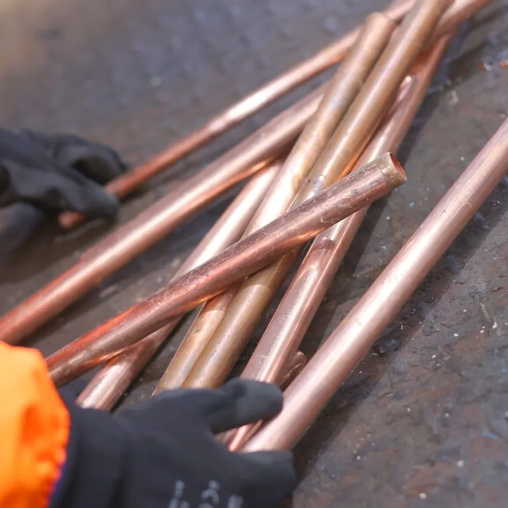A person wearing black gloves holding copper pipes on a gray surface.
