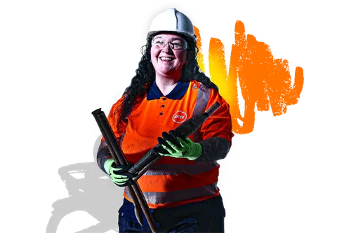 A smiling person in a hard hat and high-visibility vest holding a pipe.