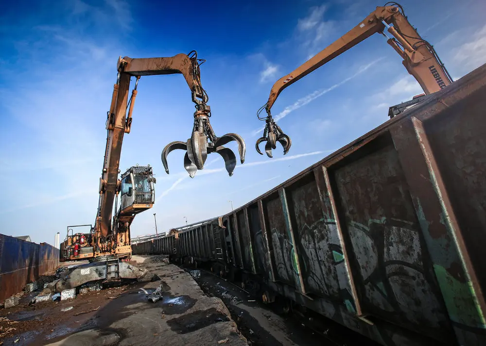 Two industrial metal grabbers actively used in a recycling facility, picking up waste material from the ground.