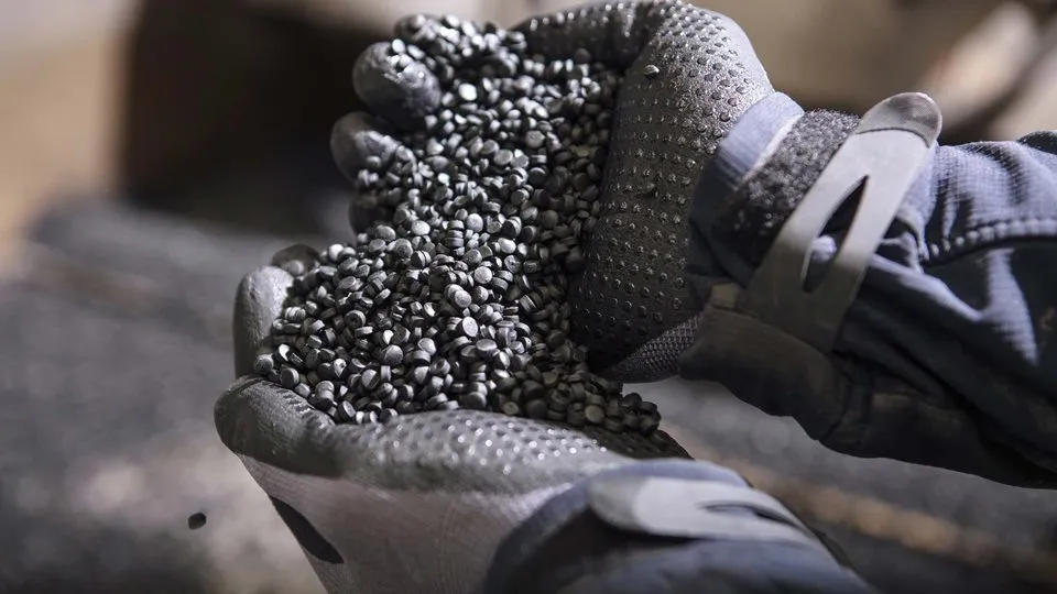 A person wearing gray gloves holding a handful of gray pellets.