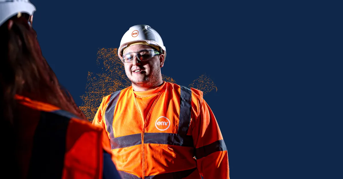 Two people in hard hats and safety vests shaking hands.