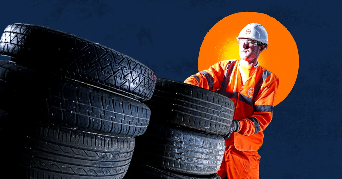 A person in a hard hat and orange jumpsuit holding a stack of tires.