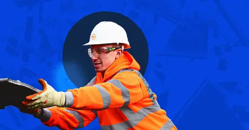 A person in a hard hat and safety gear holding a tool near a circular opening.