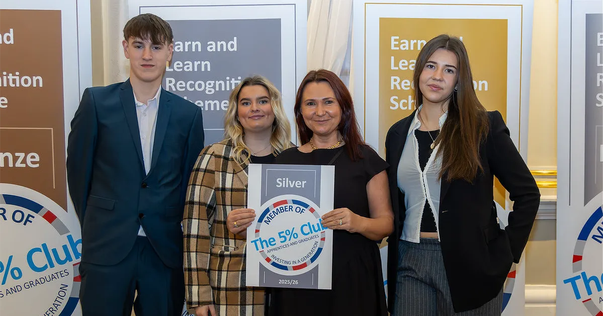 Group of four people standing indoors holding a certificate that reads ‘Silver Member of The 5% Club’ for the year 2023/24. Behind them are three vertical banners displaying text about the Earn and Learn Recognition Scheme in bronze, silver, and gold categories.