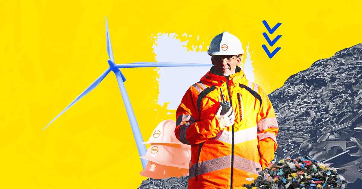 A person in a hard hat and high-visibility jacket stands in front of a wind turbine and a pile of scrap metal.